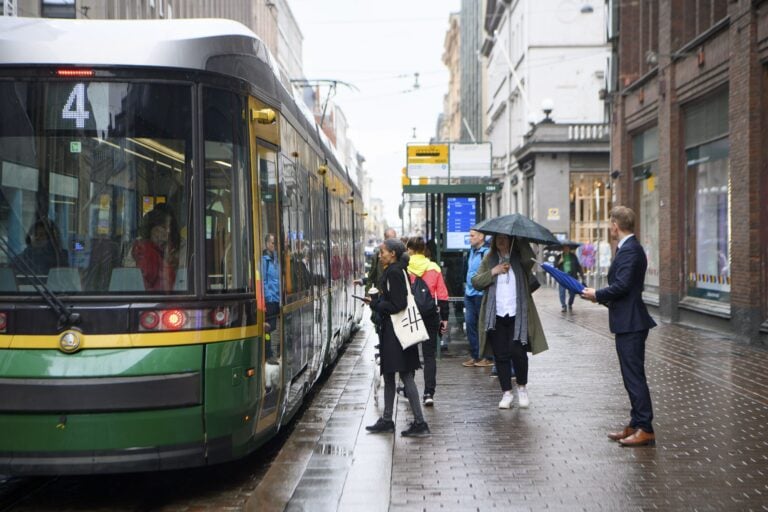 Kaupunkilaisia raitiovaunupysäkillä Helsingin keskustassa. LEHTIKUVA / ELSA PAAKKINEN